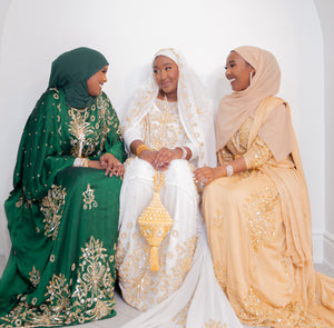 Three women wearing green, white, and gold bridal dirac sitting together.